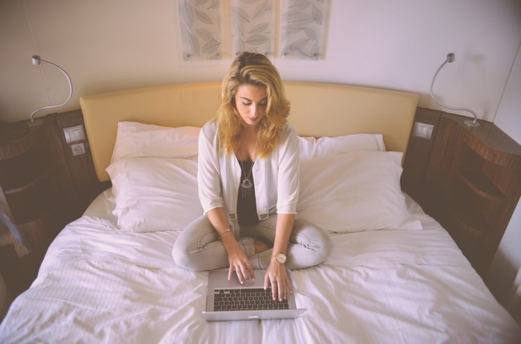 Frau sitzt mit Laptop auf ihrem Bett und lernt