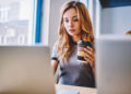 Studentin sitzt mit Kaffee vor Laptop und bucht sich in einen Kurs an der IU ein