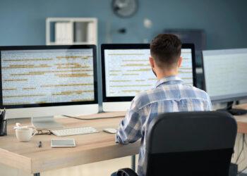 Programmierer sitzt vor großen Bildschirm am Schreibtisch bei der Arbeit, Developer Gehalt und Lohn