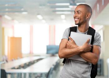 Student mit Rucksack und Unterlagen in der Hand im Hörsaal stehend