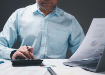 Einzelunternehmer schreibt Rechnung, am Schreibtisch mit Laptop sitzend